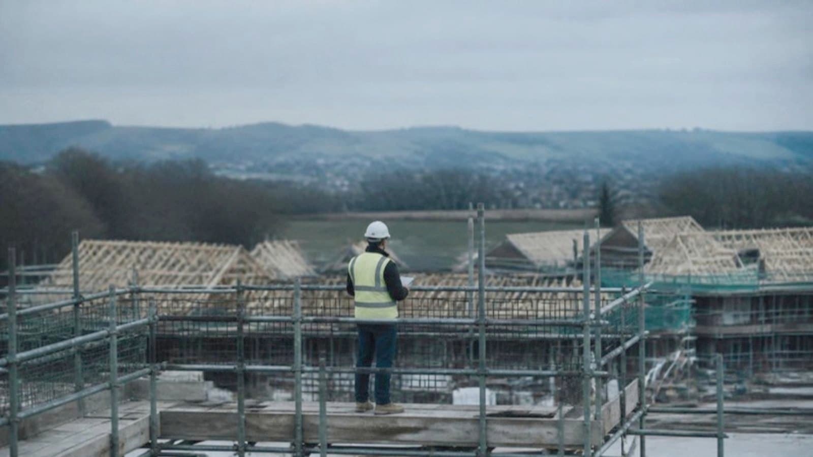 A site manager in a hard hat and hi-vis looking over a building site