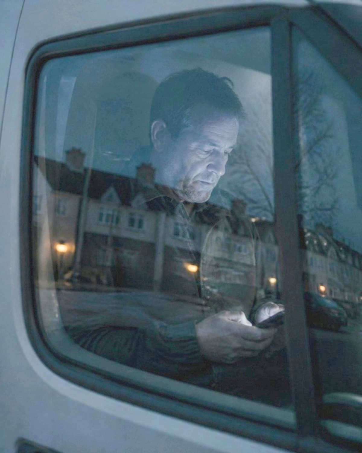 A tradesman reading his phone in his van at dusk